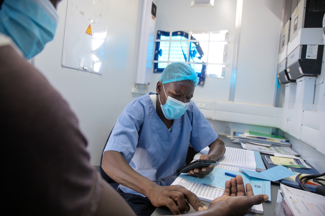 Dr. Juma Mlende counsels client Malemi Njile Igombe in the Tohara mobile clinic van, performing an HIV test and taking blood pressure prior to VMMC service. Ichila village, Busega district, Simiyu region.