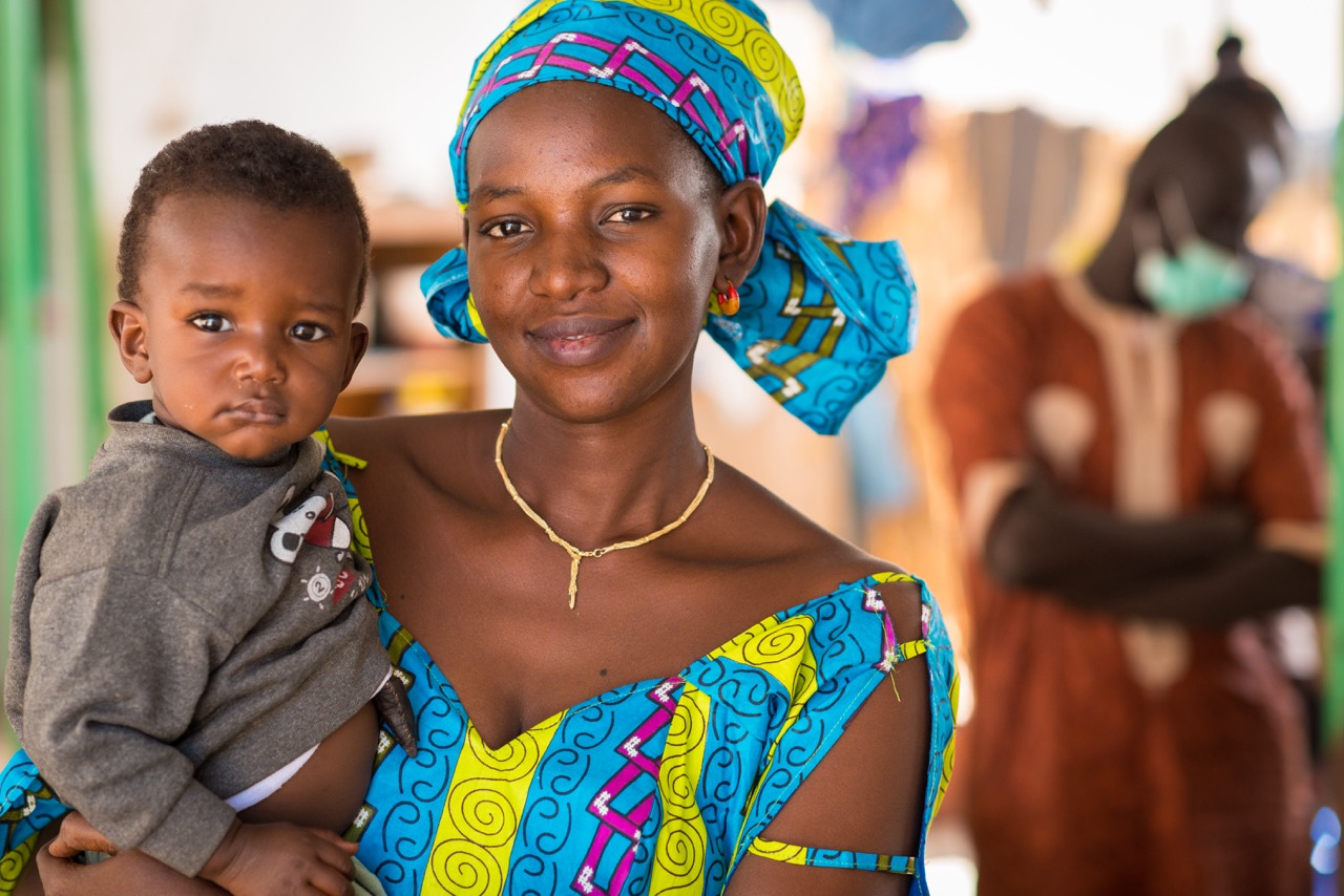 A mom is holding a child and smiling in a portrait.
