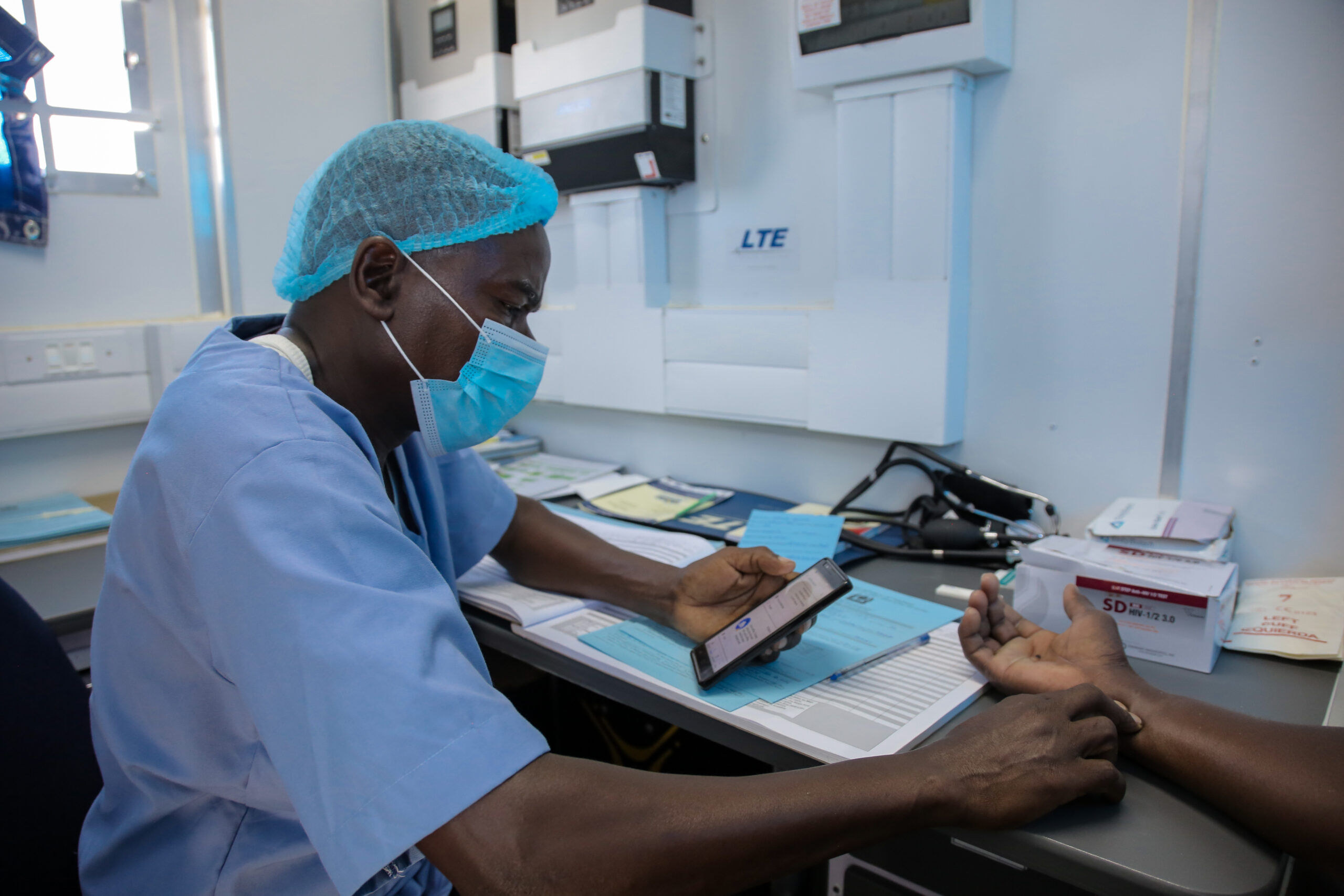 Dr. Juma Mlende counsels client Malemi Njile Igombe in the Tohara mobile clinic van, performing an HIV test and taking blood pressure prior to VMMC service. Ichila village, Busega district, Simiyu region.